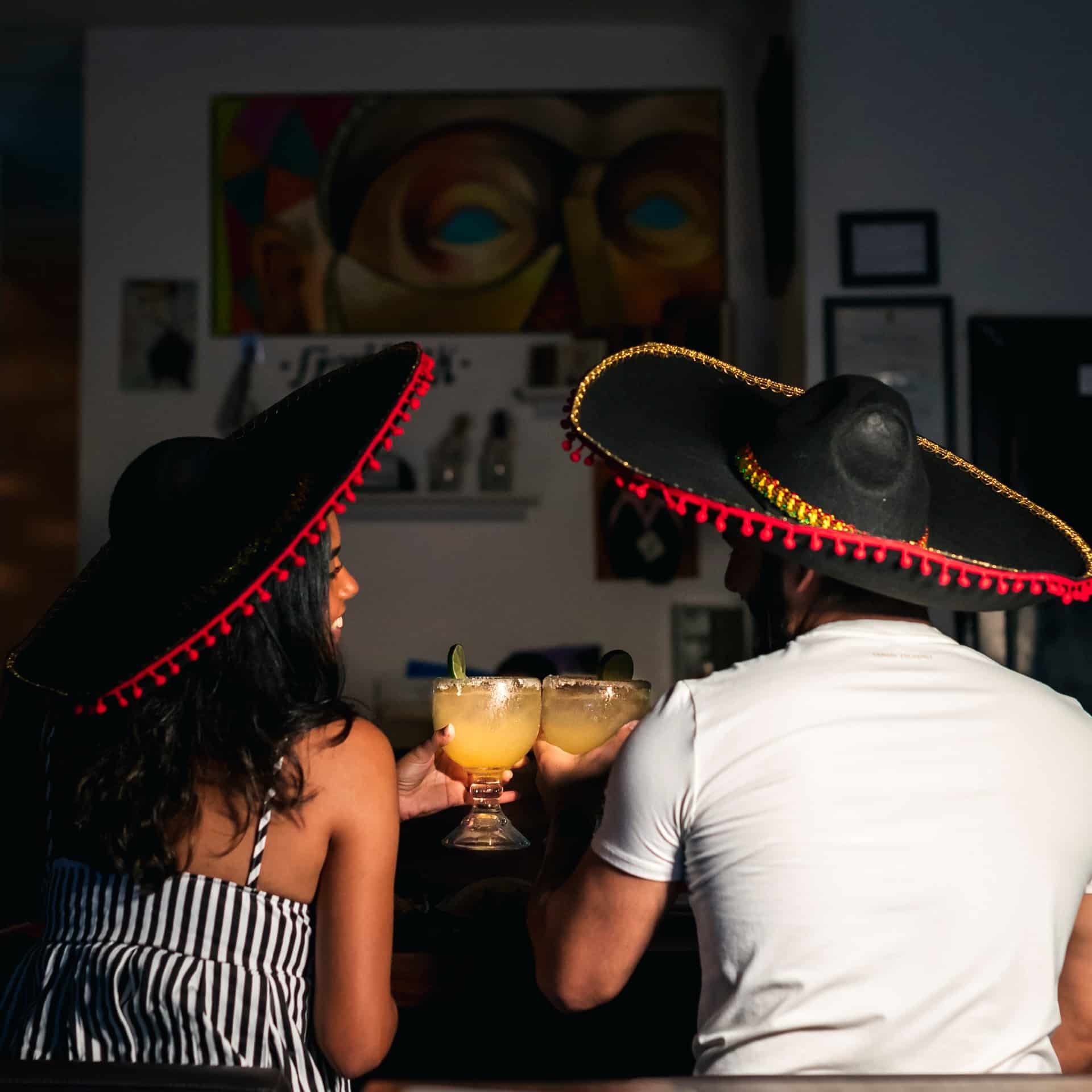 Una pareja brindando con margaritas y con sombreros de mariachi
